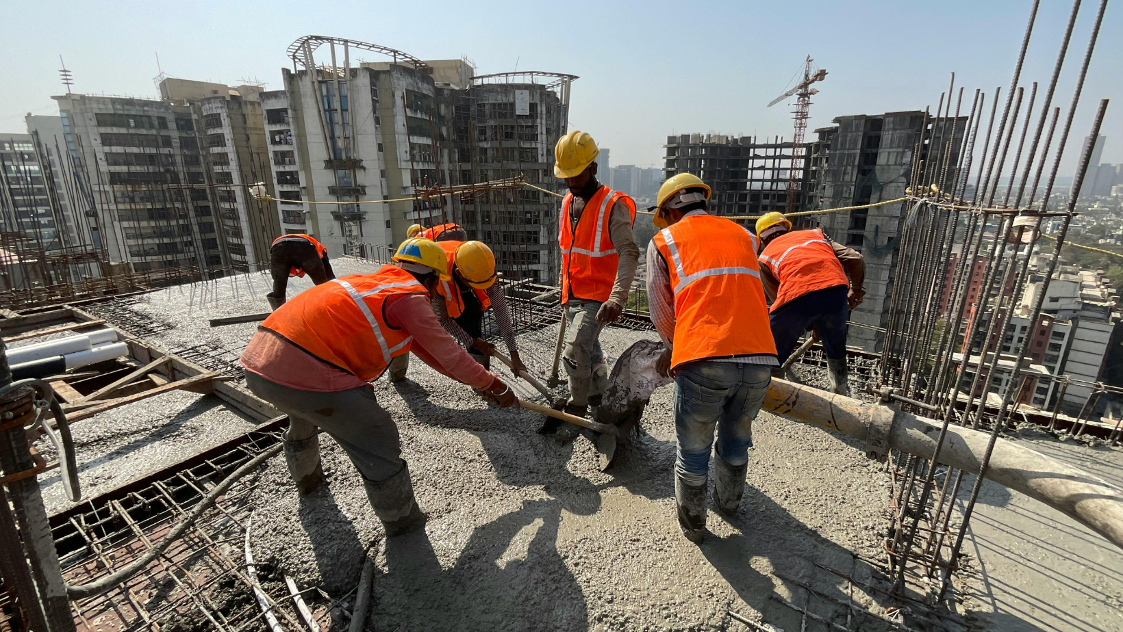 Construction crew in safety gear levelling fresh concrete on a high-rise slab